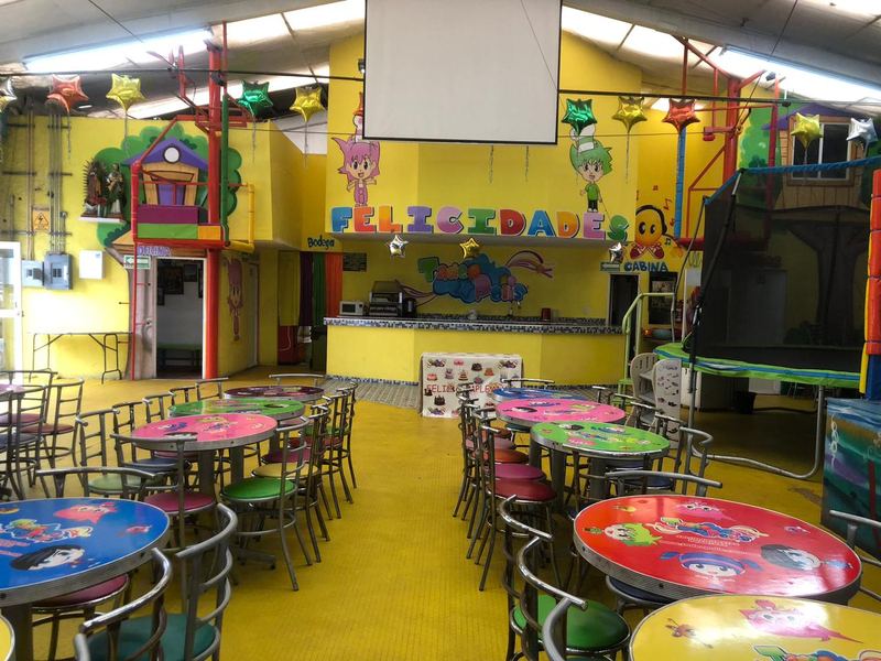 Salón de fiestas Tadeopolis con mesas infantiles de colores, barra de servicio y mural de bienvenida