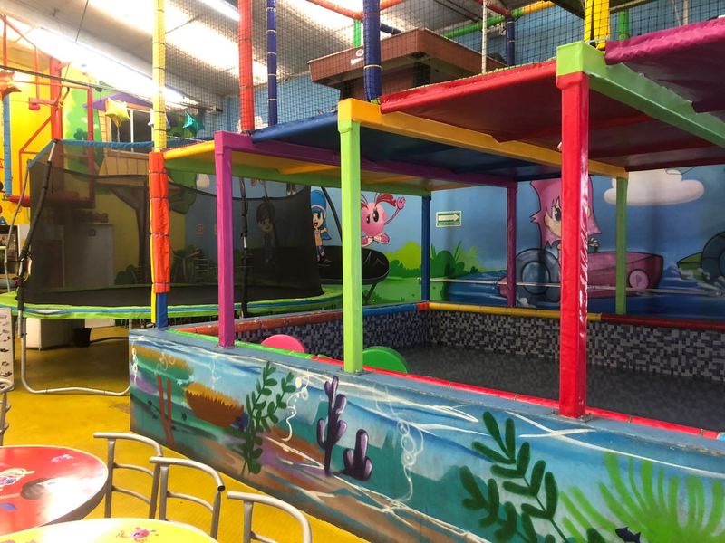 Zona de juegos techados con plataformas de colores y mural marino, junto al trampolín