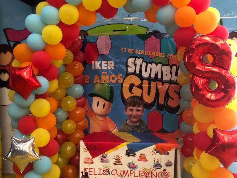 Fondo de cumpleaños con arco de globos rojo, amarillo y celeste y lona personalizada del festejado