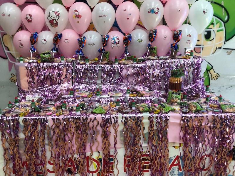 Mesa de dulces por niveles con globos rosas y blancos y cortinas metálicas